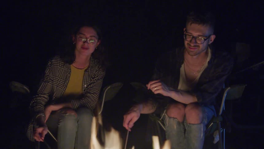 A man and a woman toast marshmallows over an open fire