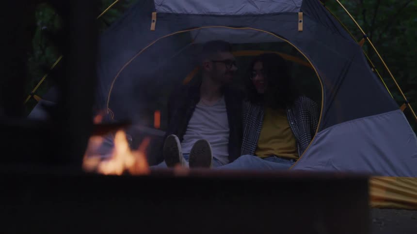 A man kisses a womans forehead in a tent next to a campfire