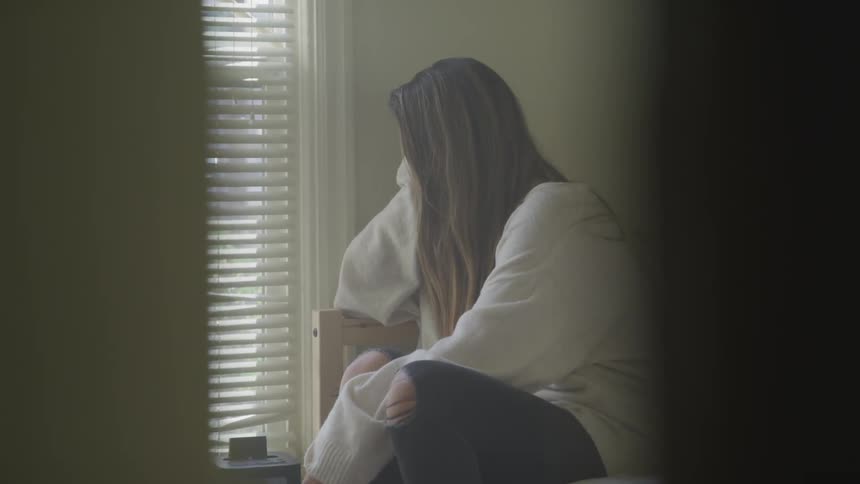 Woman sitting on the bed looks out the window in a room