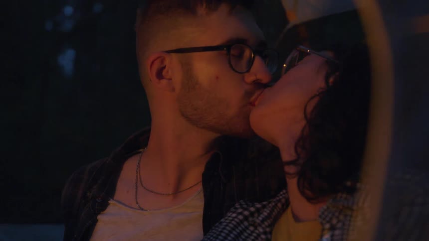 A young man and woman sit outside and kiss