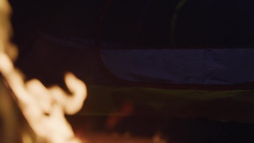 In the darkness of night a fire burns next to an object covered in fabric