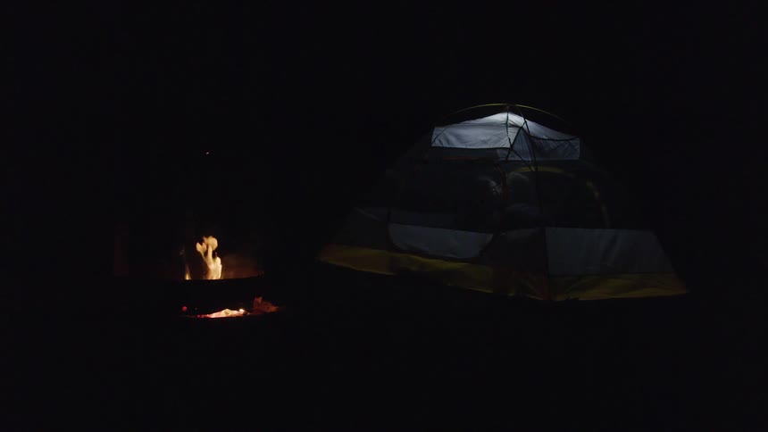People kissing inside a tent at night with a fire burning outside