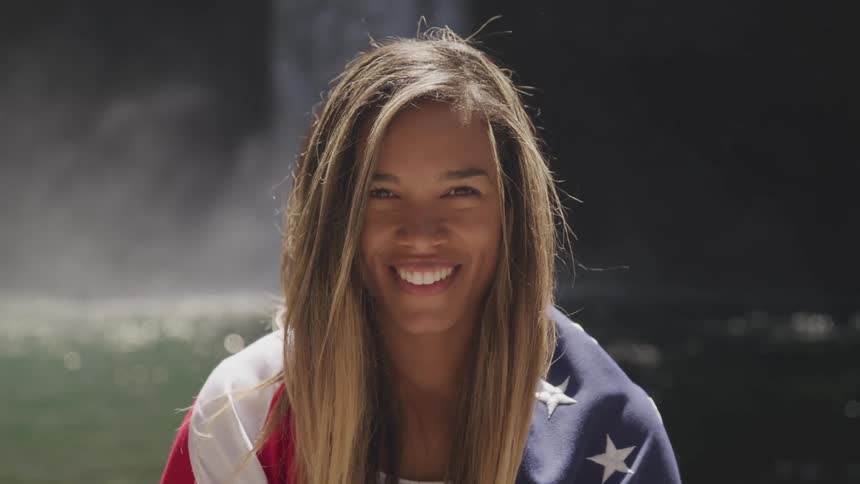 A young girl sits with a flag over her shoulders and smiles