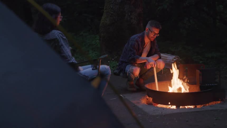 Young couple sitting around a campfire near tent in the woods
