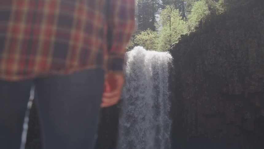 A person stands and looks at a waterfall flowing over a cliff
