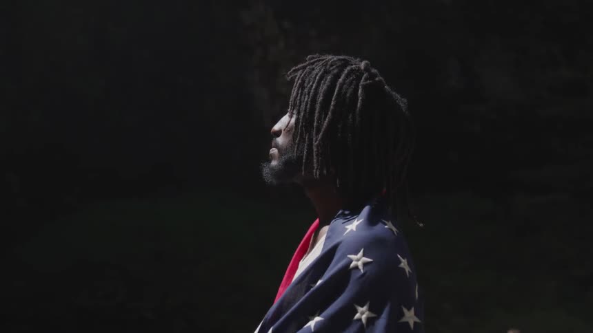 A black man wrapped in an american flag looks off into the distance