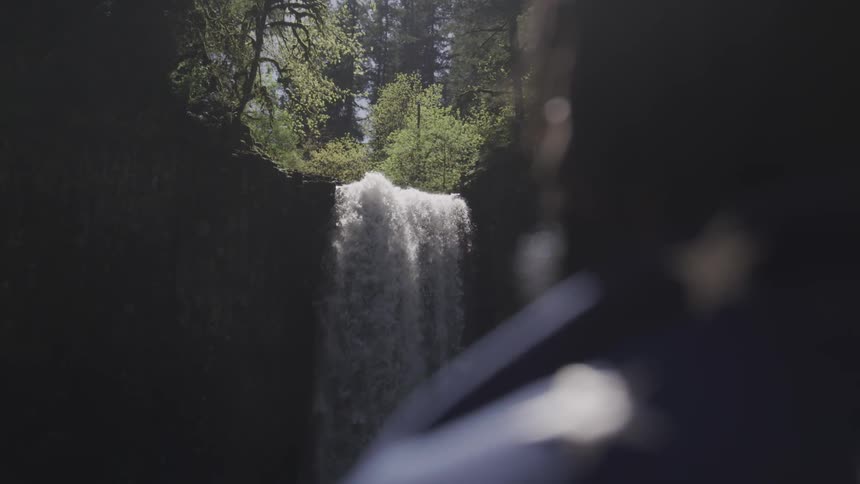 A person standing draped in an american flag looking at a waterfall