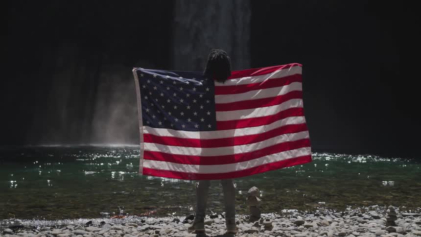Man wearing the united states of america flag standing in front of lake and waterfall