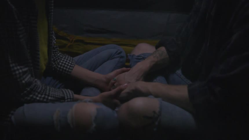 A man and a woman sit cross legged on the floor and hold hands