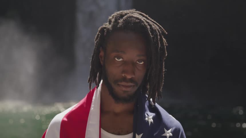 Man wearing the united states of america flag stands in front of lake and waterfall