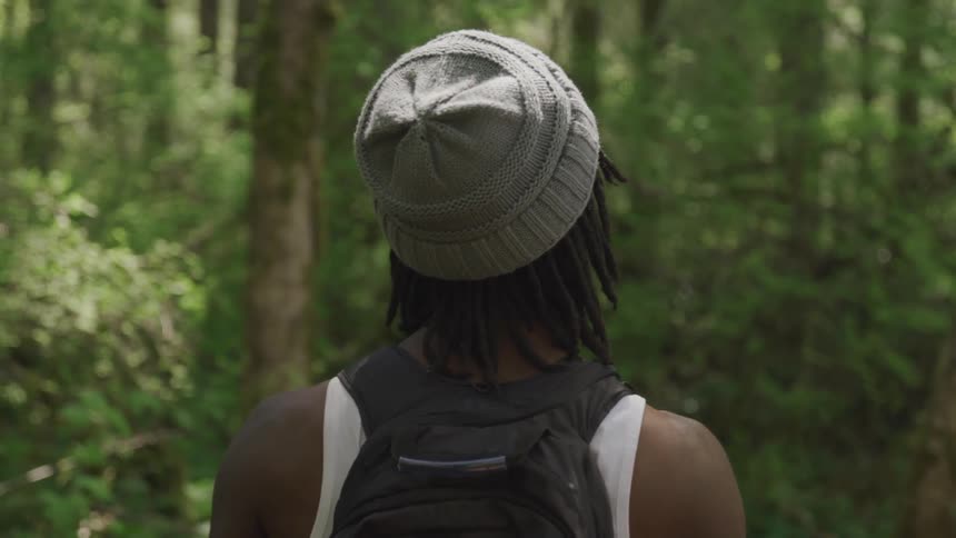 Man wearing a backpack and toque walks in the forest on a sunny day
