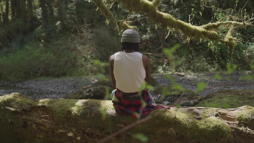 Black man sits on the tree trunk in the forest