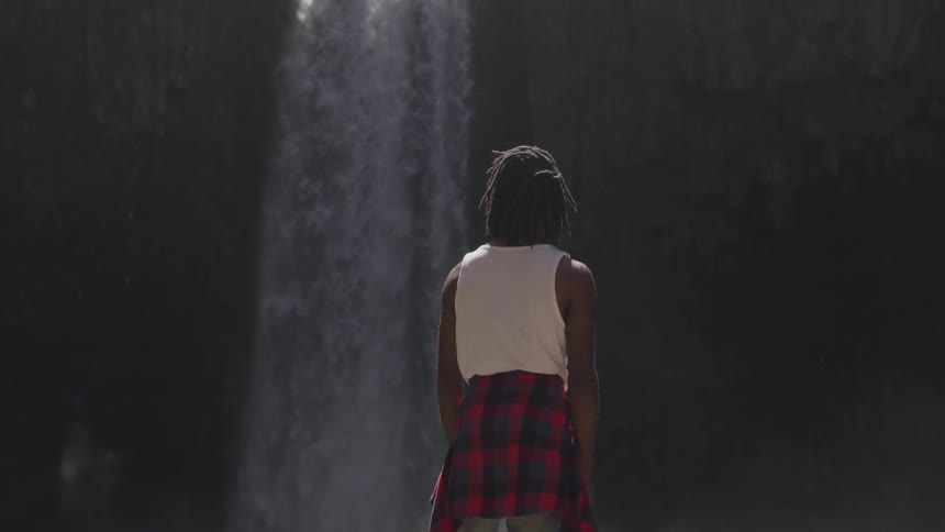 A young girl stands and looks at a waterfall