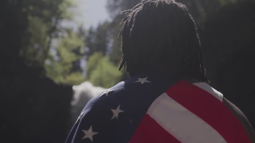 A man is standing by a waterfall with an american flag on his back