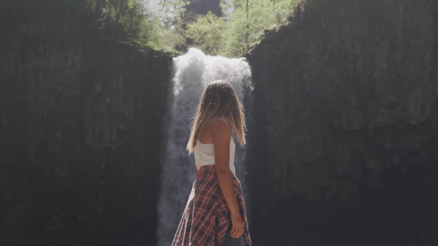 A woman stands at the base of a waterfall