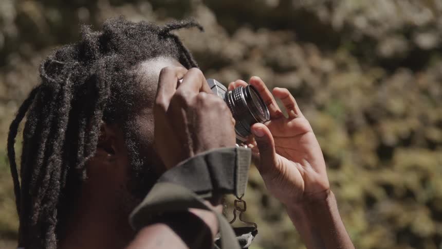 A man lifts his camera and focuses it to take a photo outside