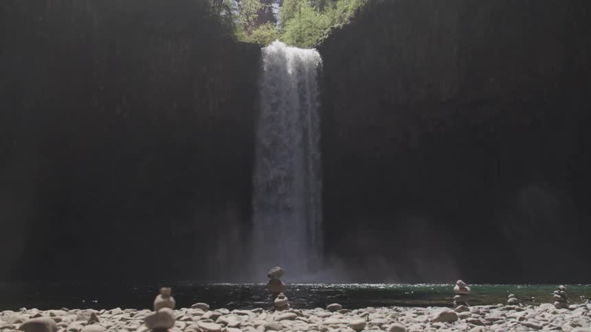Rocky ground sits next to a lake being filled by a large waterfall