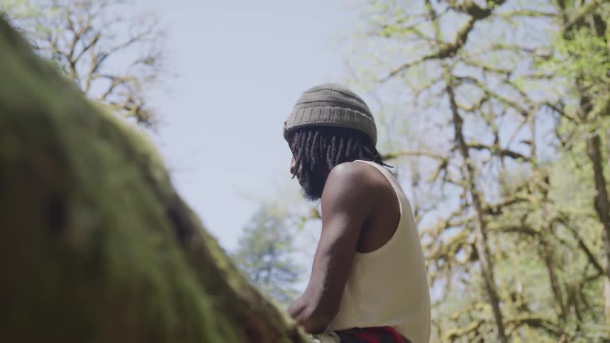 A man sits alone on a log in the forest