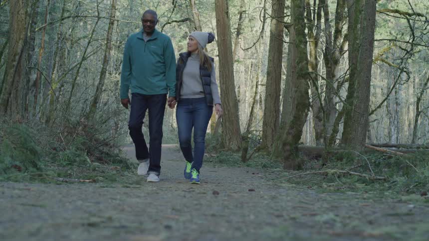 A man and woman walk along a forested path holding hands
