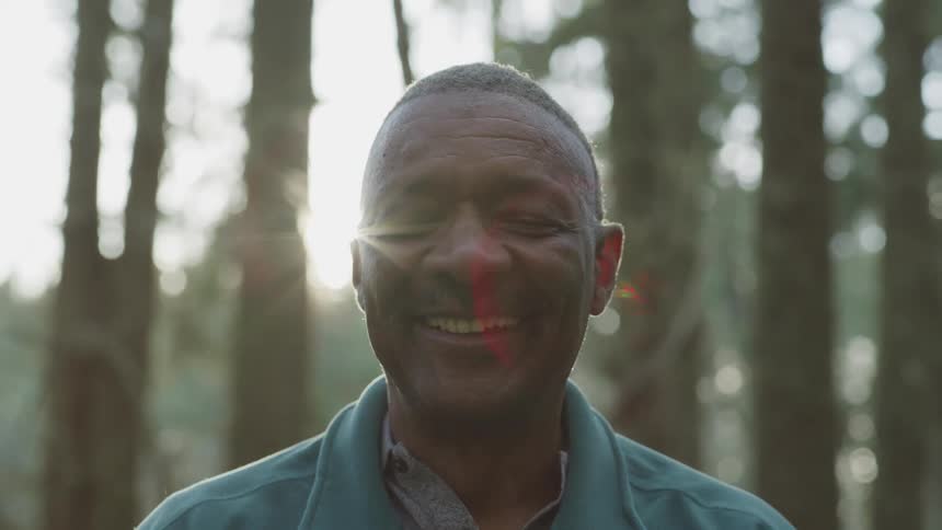 A man stands in front of trees on a sunny day and smiles