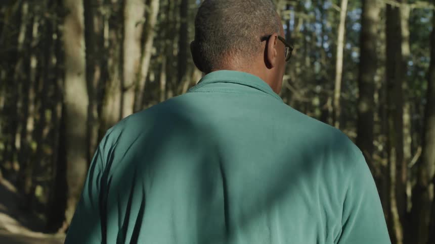 A man in glasses walks by trees in a forest