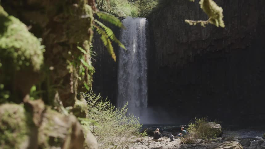 People sit on shore next to pull at base of waterfall