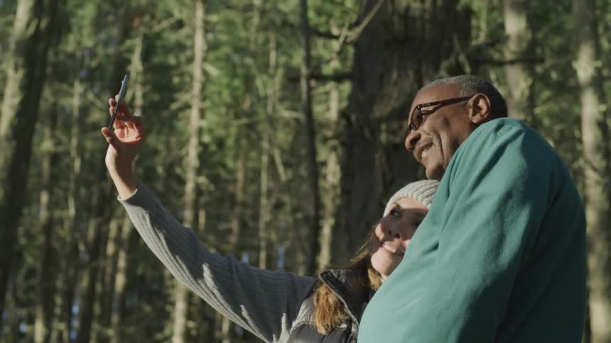 A man and woman in a forest embracing to pose for a selfie