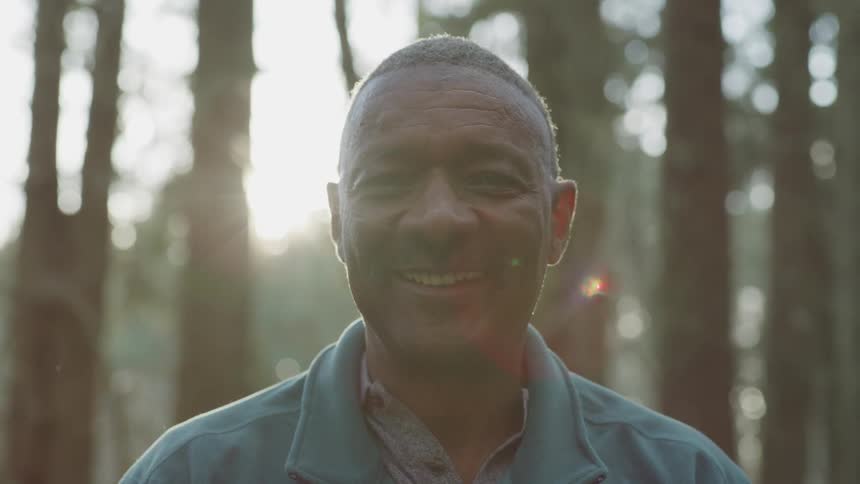 A man standing in the woods staring and smiling