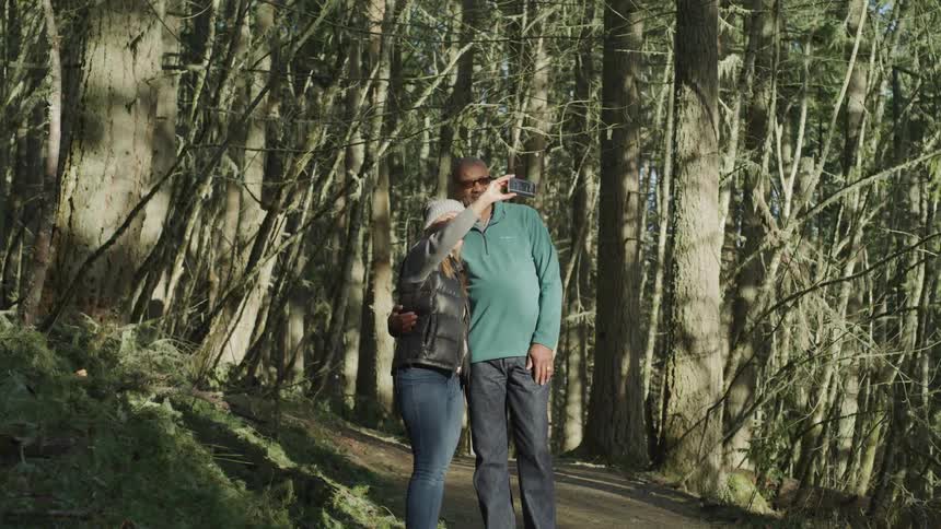 Middle aged couple standing on a trail in the forest taking a selfie