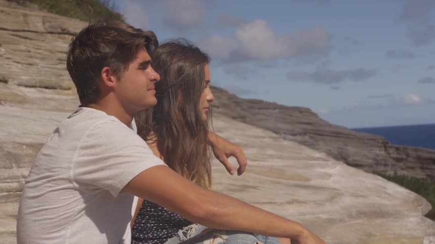 Couple sitting on a cliff looking at view of the beach