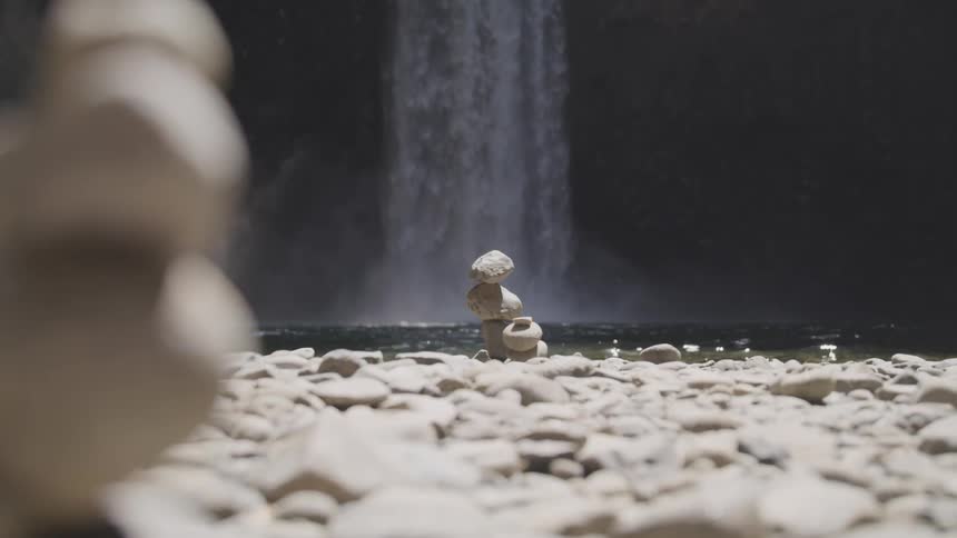 A rocky shore with stones stacked up with a waterfall in the background