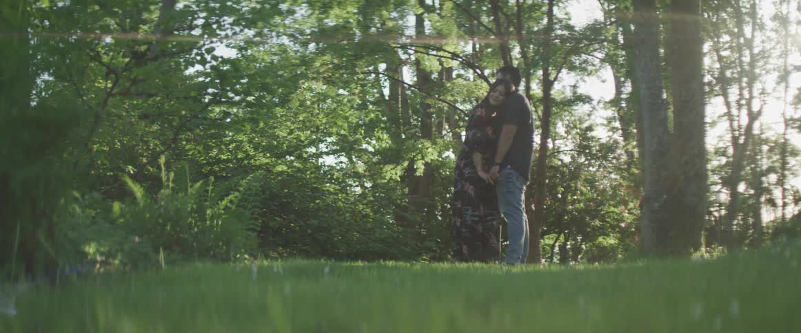 A man and woman hug while standing near trees on a summer day
