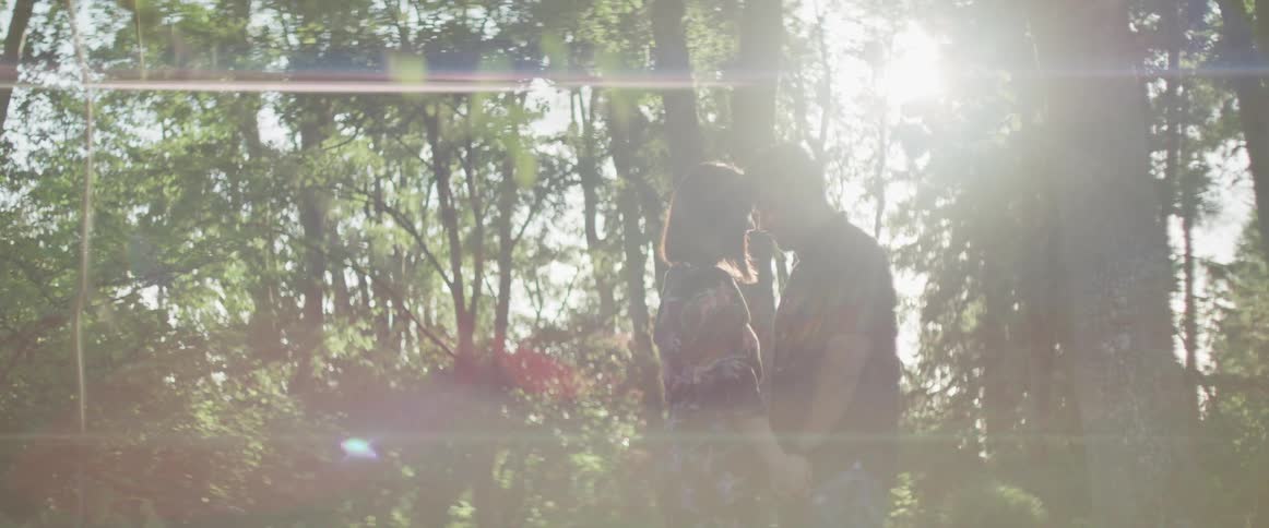 A couple stands near the trees holding hands with foreheads touching
