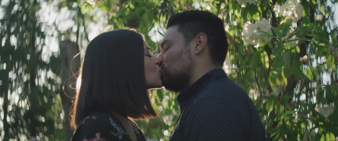A man and woman kissing in front of a tree