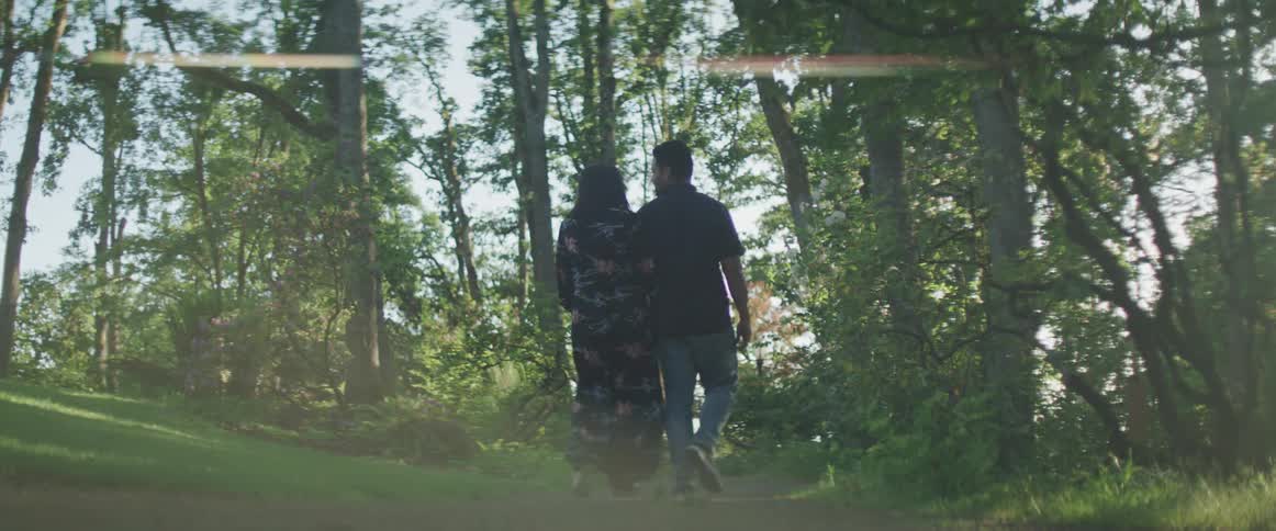 A man and a woman walking on a path in the woods holding hands