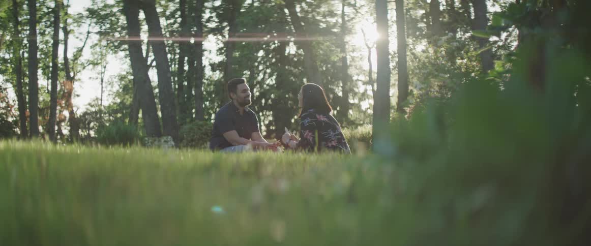 Man and woman sit on the lawn and talk to each other while the sun streams through the trees
