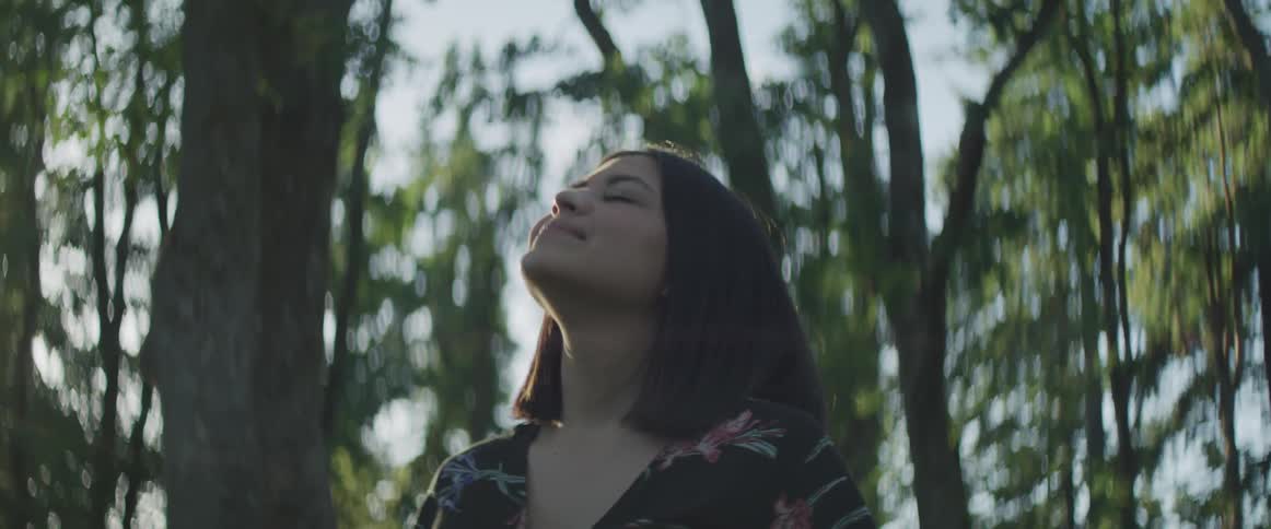 Woman looks towards the sky as she stands in a forest on a sunny day