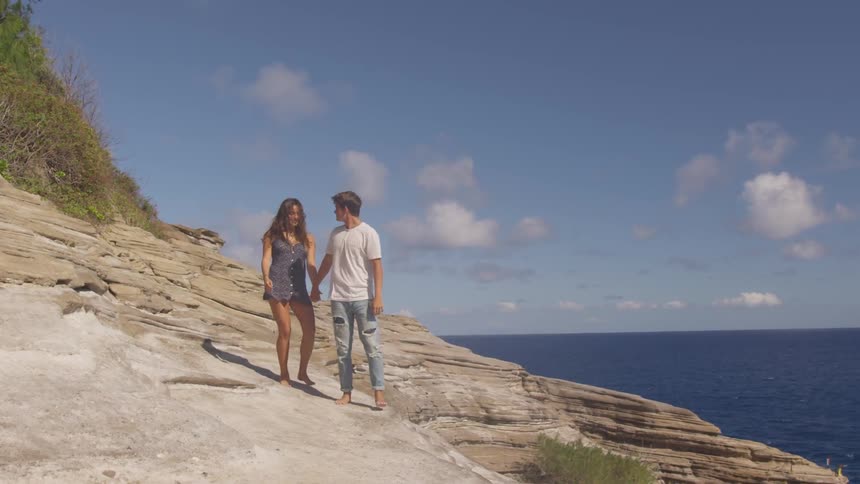 Couple walking barefoot on a cliff near a beach