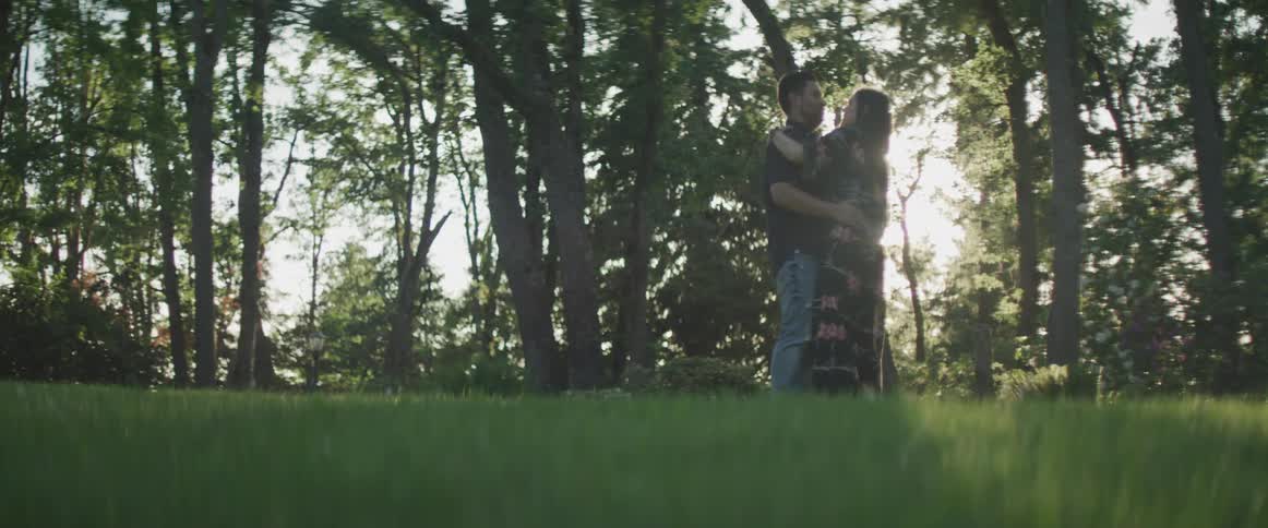 A man and woman slow dance near trees on a sunny summer day