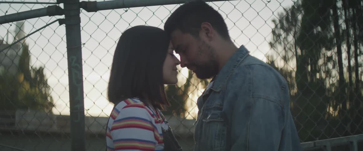 Man and woman touches heads in front of the wire fences at dusk