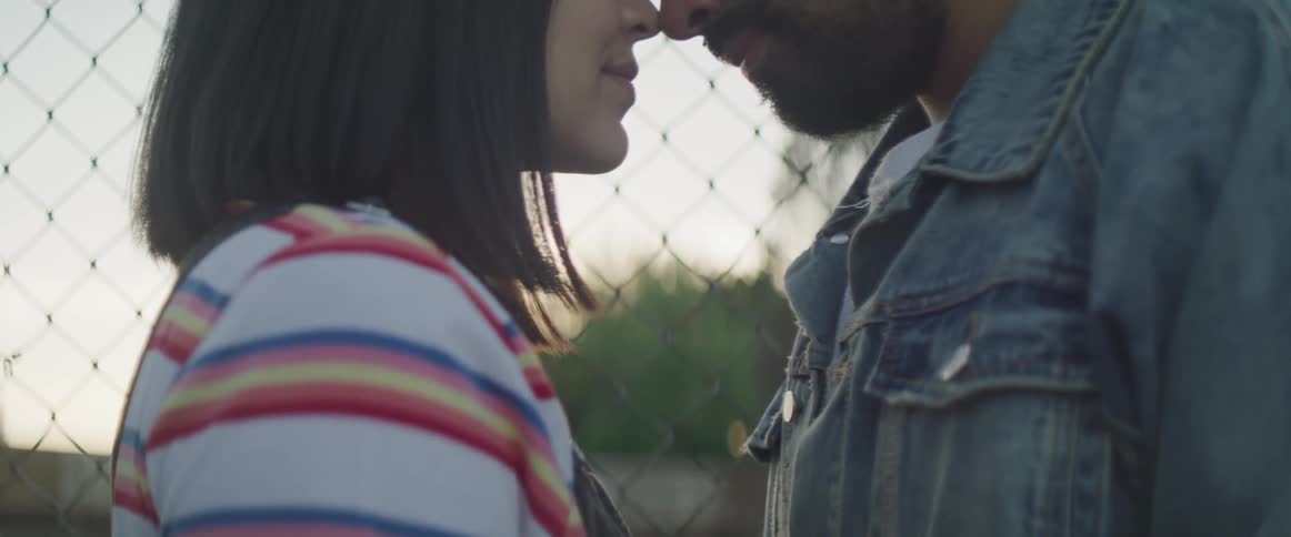 A young woman and man stand outside with their noses together