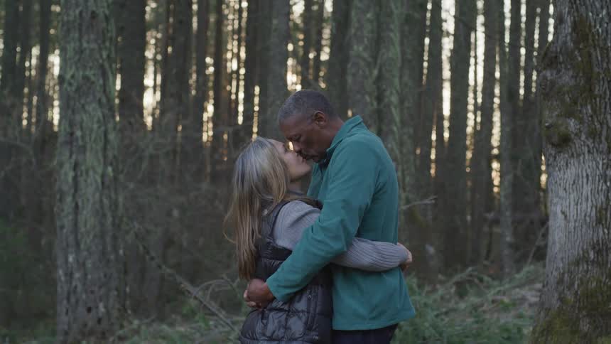 Black man and blonde woman hold and kiss each other in the forest