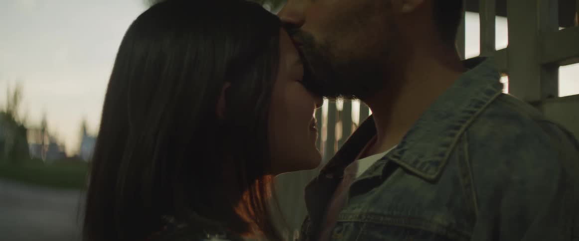 A man kissing a woman on the forehead while the two stand outdoors