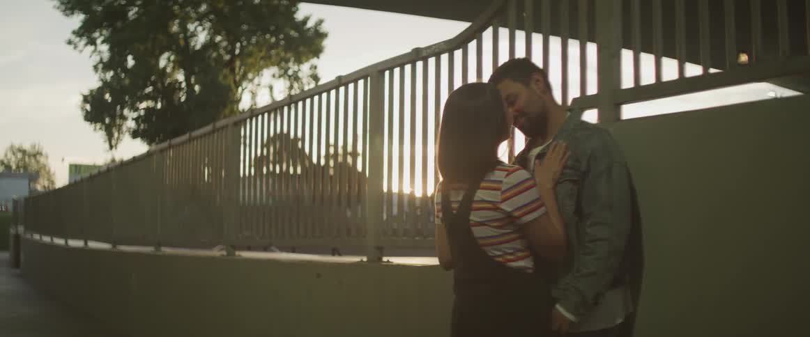 A man and woman kiss outside at sunset