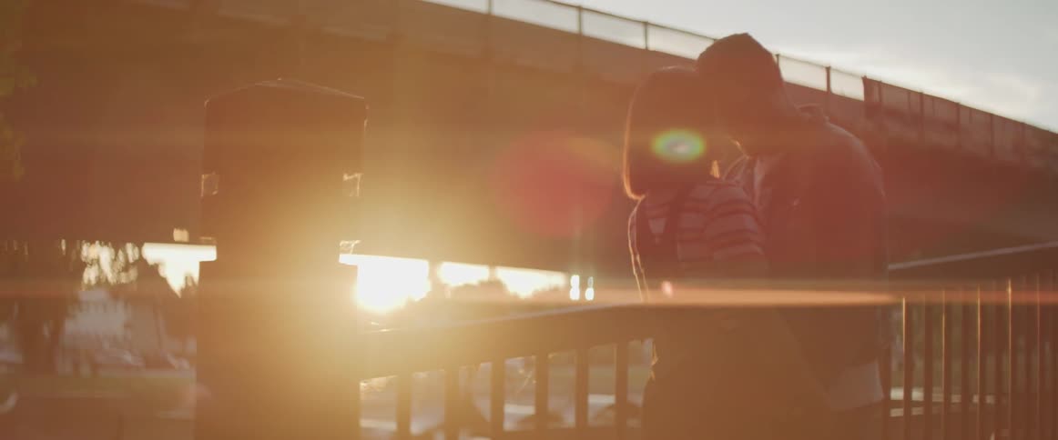 A man and a woman lean in close to each other while standing on a ramp outdoors