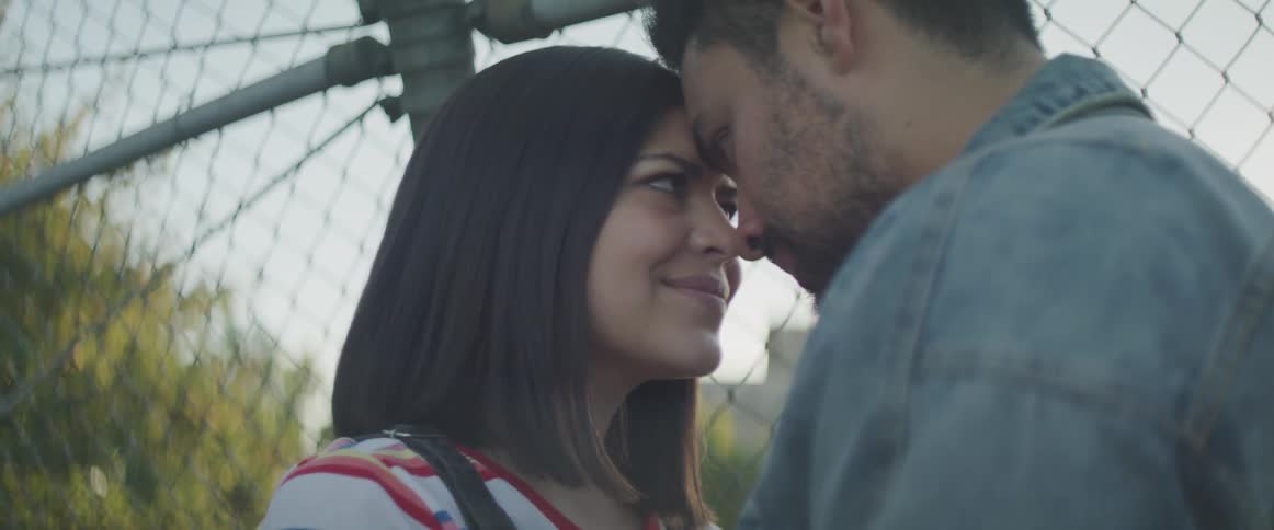 A man and woman rest there foreheads together beside a fence