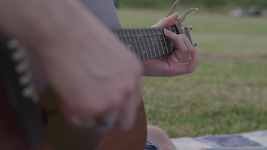 A man plays a guitar sitting on a blanket in the grass