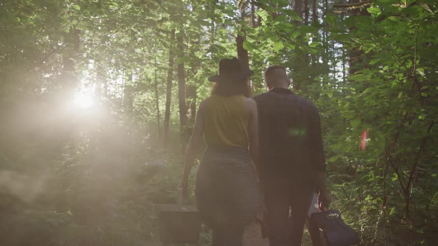 A couple walk through the woods at sunset