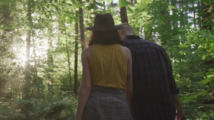 A man and woman hold hands while walking through the woods