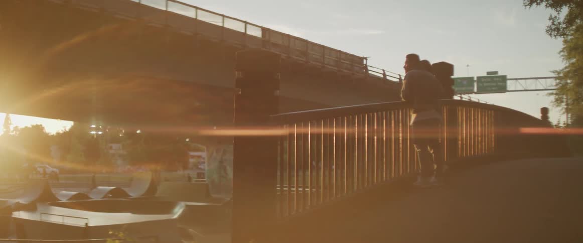 Man and woman lean against a railing as they look at the river under the bridge